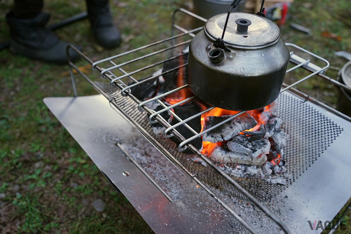 別売の五徳（ひとつ4500円。写真はふたつ使用）を使って焚き火料理。五徳はフレームにしっかり噛み合ってずり落ちないようになっている。専用五徳を使わない場合は、火床をスライドさせて火力調整できるのがおもしろい