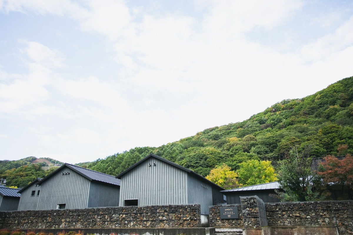 山の緑を背に、蔵を思わせる建物と石壁が連なる