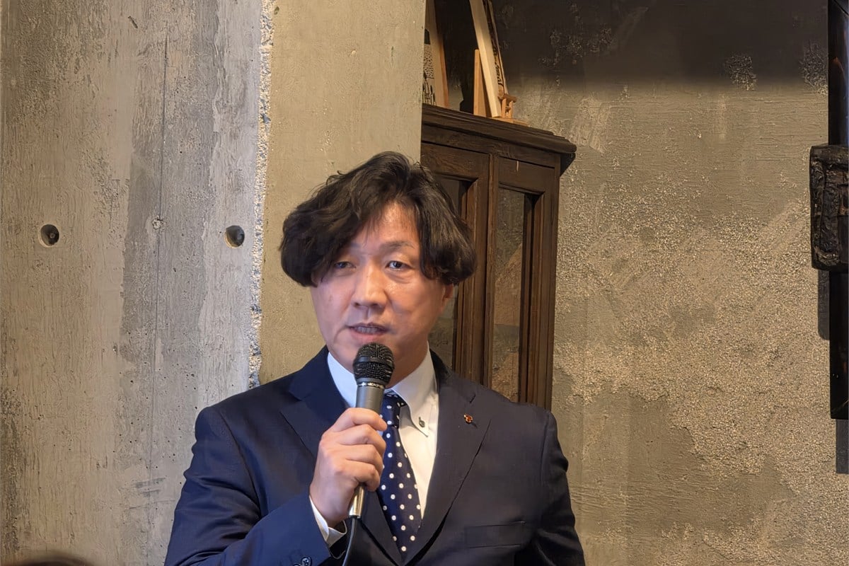 土鍋炊飯器20周年プロジェクトの背景を説明するタイガー魔法瓶 執行役員 ソリューション本部長の岡本正範氏。タイガーは、工芸品である土鍋を精度が求められる工業製品に組み込む難しさと、それでも採用し続けてきた理由を紹介した。