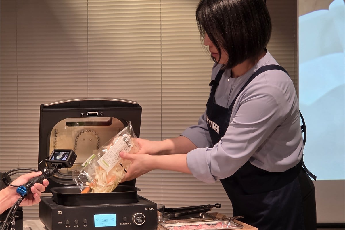 タイガー魔法瓶のソフト担当者が、焼きそばの実演でインナーポットに野菜を入れているところ。麺、野菜、豚肉の順に重ねて加熱し、仕上げにソースを混ぜる。フライパンで炒め続けなくてよい手軽さが印象的だった。