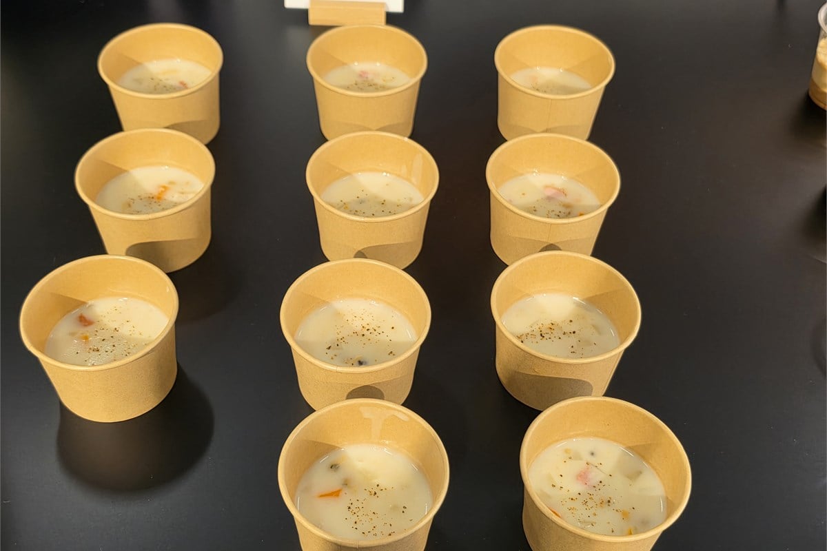 クラムチャウダーの試食用カップが並ぶ会場。新型では、具材を必要以上に砕かずに加熱する「ごろごろスープ」の制御も見直した。温かい料理でも食材の形を残すなど、仕上がりに応じて攪拌方法を使い分ける。