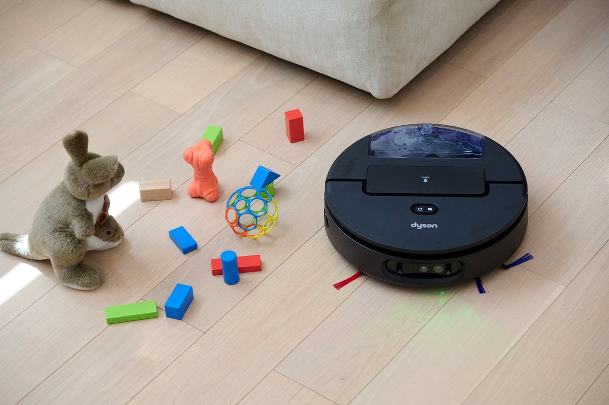 ぬいぐるみやブロックなど、床に散らばった障害物を前にした実使用イメージ。AIカメラとグリーンLEDを活用し、家庭内の複雑な環境を認識しながら掃除することを訴求している
