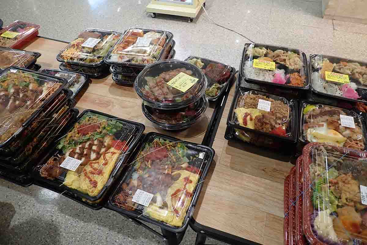 「コンビニ シャロン」の店頭のテーブルには、お昼どきにお弁当が所狭しと並べられる。500円以下のお弁当もある