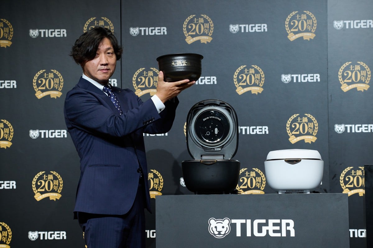 発表会に登壇したタイガー魔法瓶 執行役員 ソリューション本部長の岡本正範氏。手にしているのは、約3か月をかけて作られる本物の土鍋釜。20年にわたって同社が磨いてきた“土鍋”技術の象徴だ
