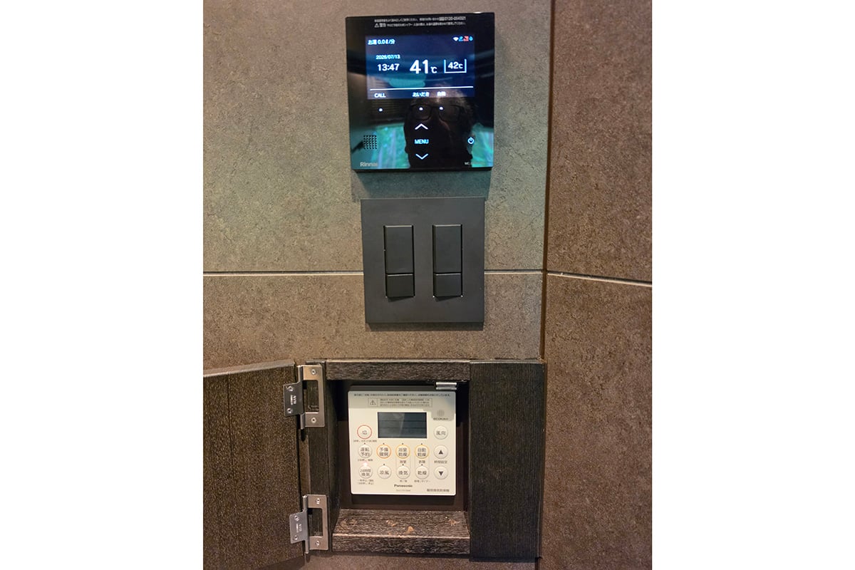 黒でそろえられたお風呂の給湯スイッチ類と照明などのスイッチプレート。その下の白い給湯操作部は扉の中へ収め、必要な機能を確保しながら、使わないときには視線を止めない細部まで設計している